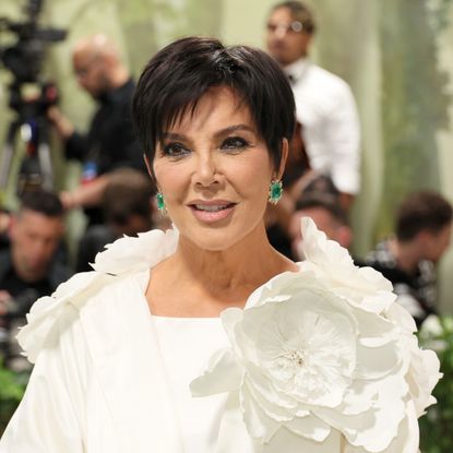 a paparazzi photo of a white woman with short, black hair wearing a white gown with a flower attachment