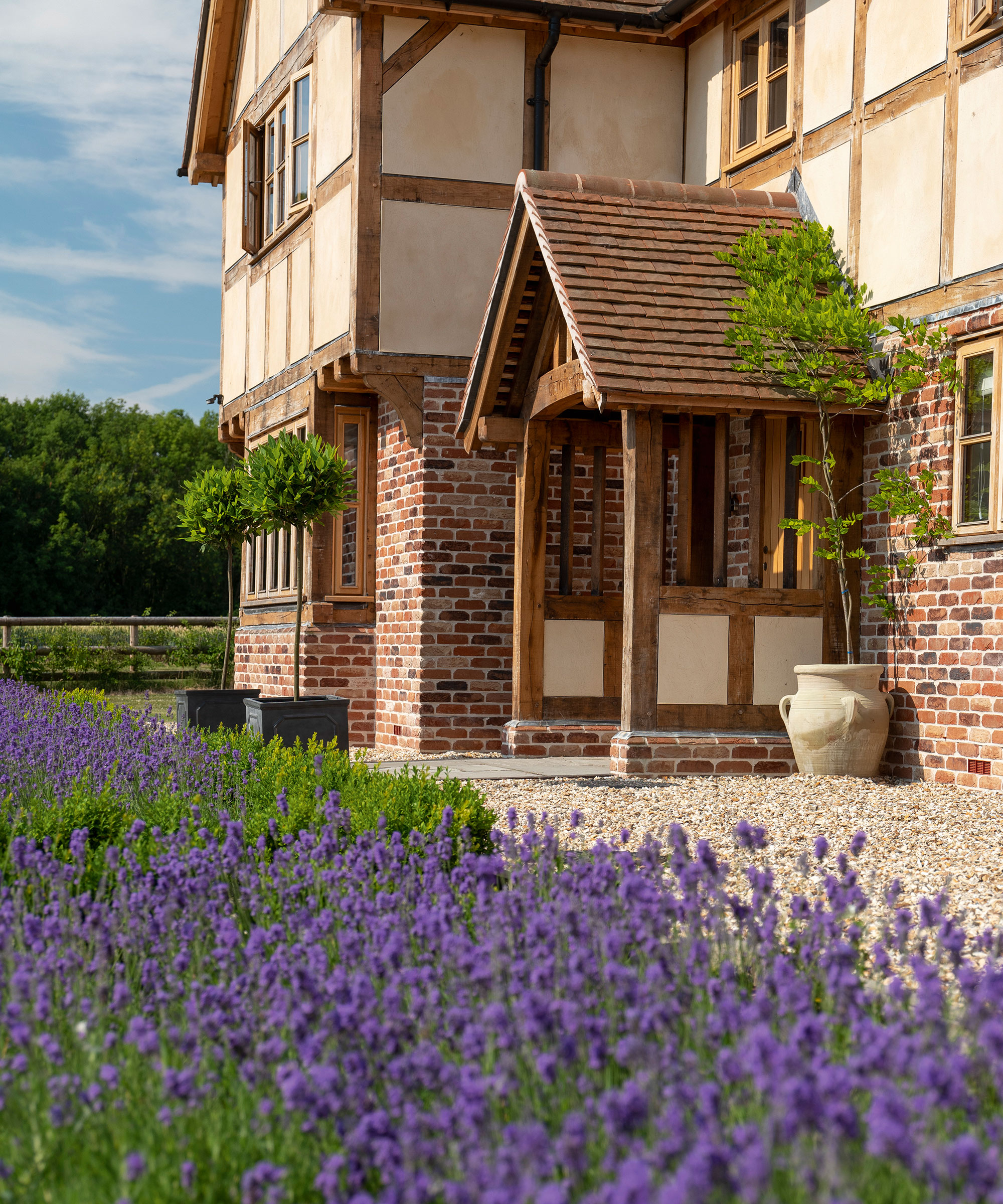 Oak frame house with a gravel driveway and borders of purple-flowering lavender in bloom