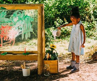 young girl playing at a painting easel in a backyard
