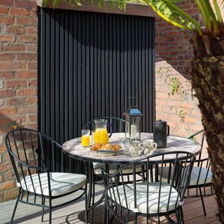 Corner of a garden with walls and cladding in front of a round bistro set