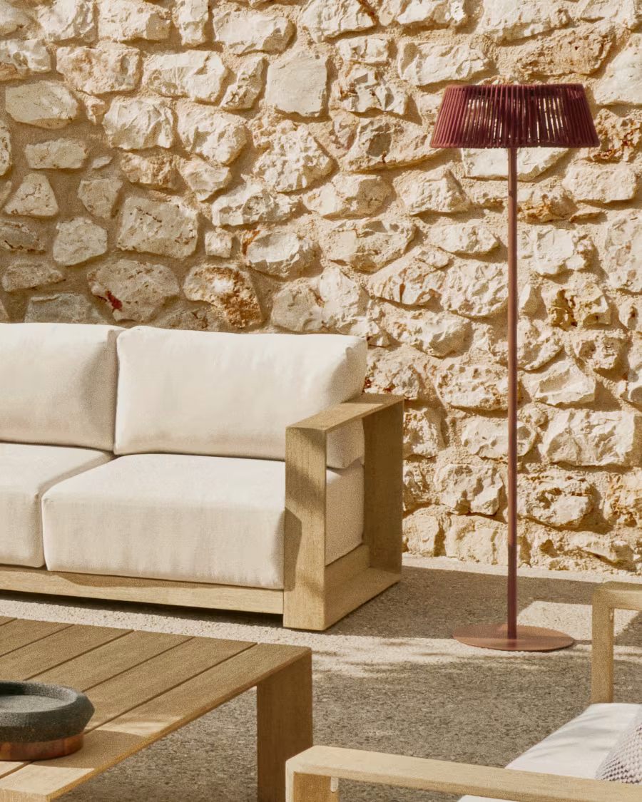 outdoor sofa in front of stone wall, with timber coffee table, and red outdoor floor lamp