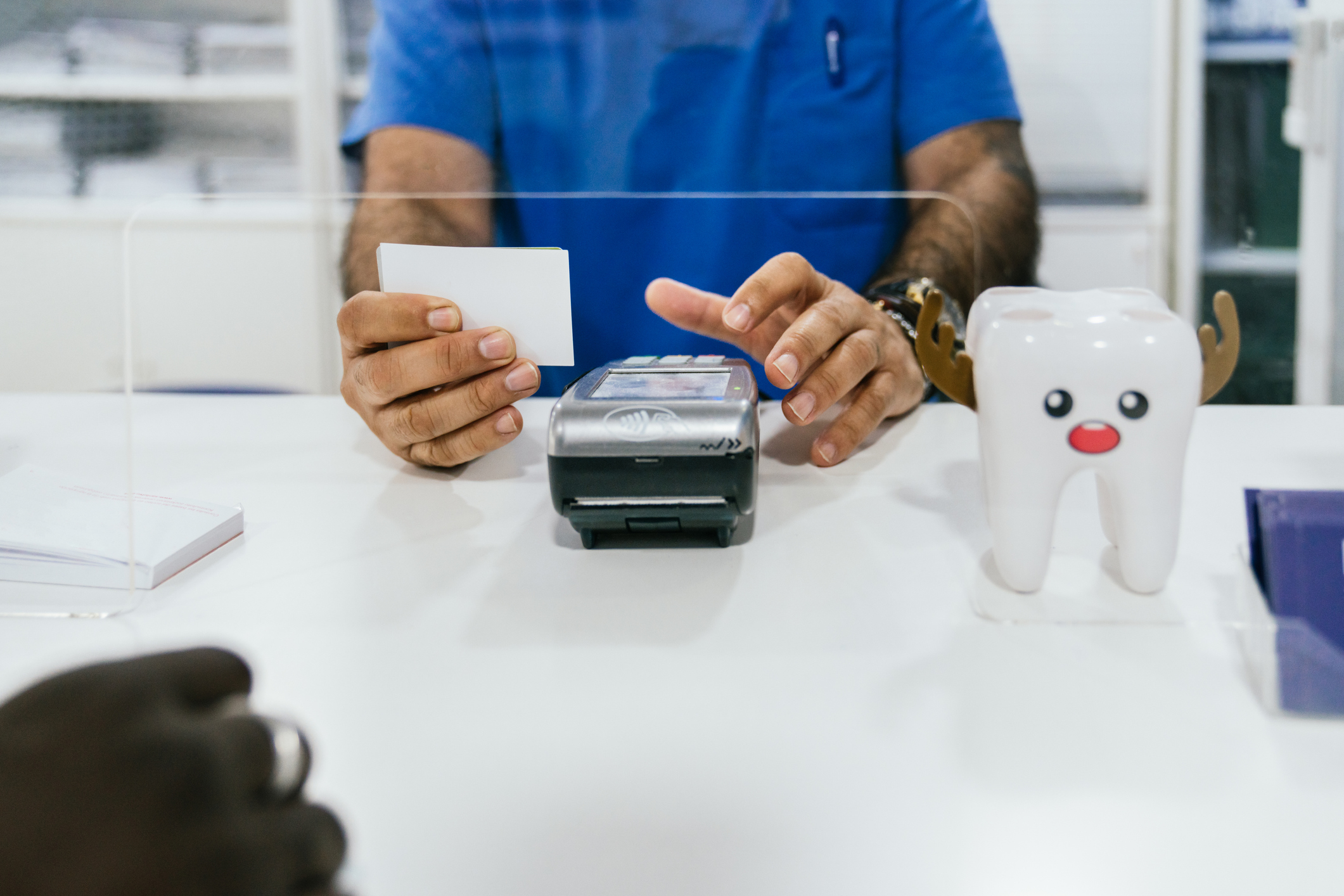 Close-up of the hands of an anonymous teller using a bank terminal to charge for dental medical services with a credit card. Take detail of a receptionist processing a card payment at a dental clinic.