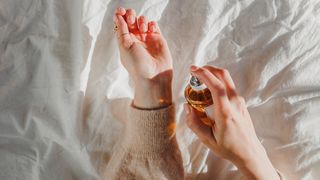 A woman applying perfume to her wrists in bed