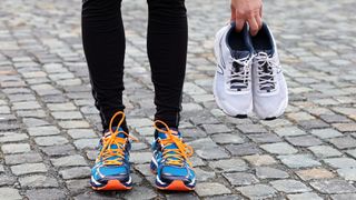 Person wearing old running shoes and holding a pair of new running shoes