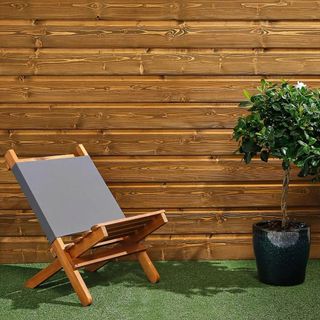 Dark wood outdoor cladding on wall with garden chair and grass.