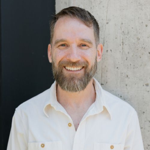 Image of a man with a beard in a white button down shirt.