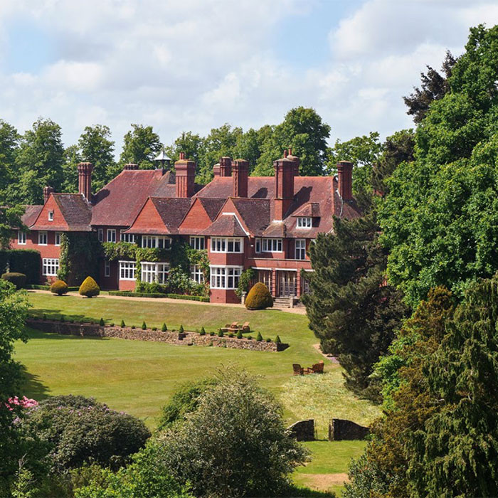 brick red sloping roof house with chimney stack and green trees