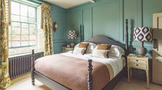 Green paneled bedroom with brown wooden ornate bed with half-height posts, and a large Crittal window in sage. The yellow patterned curtains are floor-to-ceiling height.