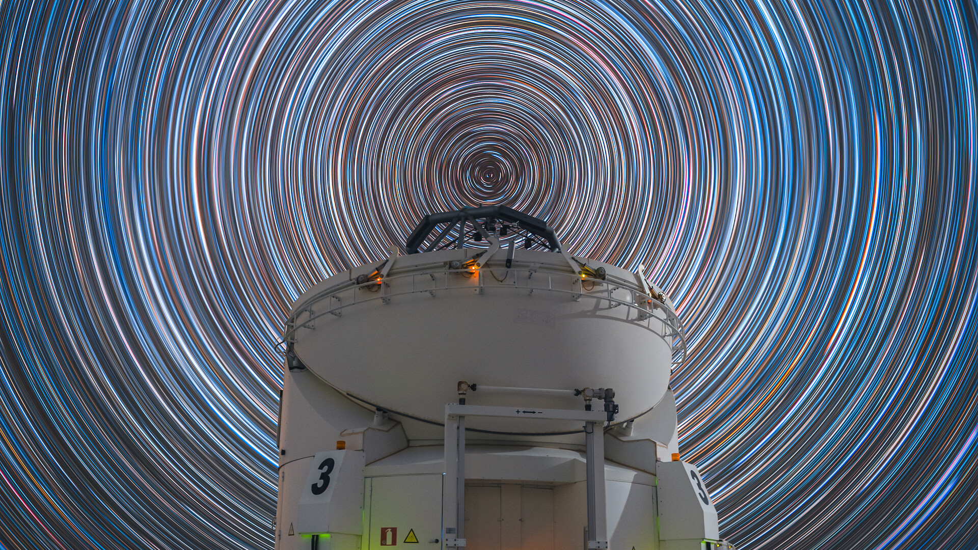 A dizzying array of concentric blue and red and white circles are seen in the night sky behind a domed white building