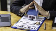A businesswoman tents her hands over the top of a plastic house that sits atop an insurance form.