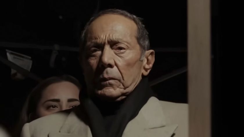 Paul Anka looking in a mirror, wear a light tan over coal and black scarf