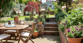 long narrow garden with a small patio area with wooden table and chairs with an elevated lawn with a wooden garden bench and green painted summerhouse