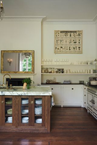 A kitchen with a wooden island, marble countertops, and open shelving displaying glassware