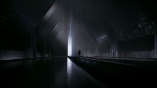 Silhouette of a person wearing a cape walking down a long dark corridor with very high ceilings.