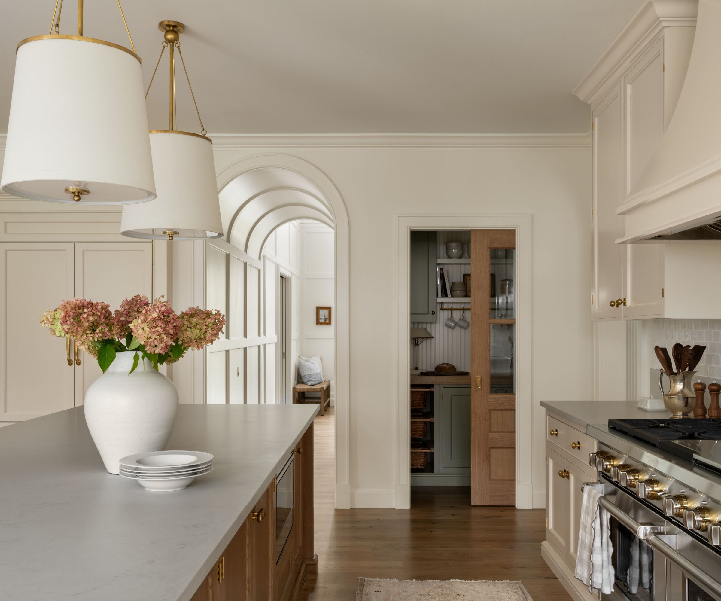 A warm neutral kitchen with off-white cabinets, a wooden island, and arched details