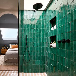 a shower area with emerald green tiles a clear glass shower panel and black hardware beside a doorway leading into an loft bedroom with roof window