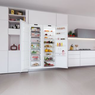 White kitchen units with open fridge and freezer with neatly organised shelves
