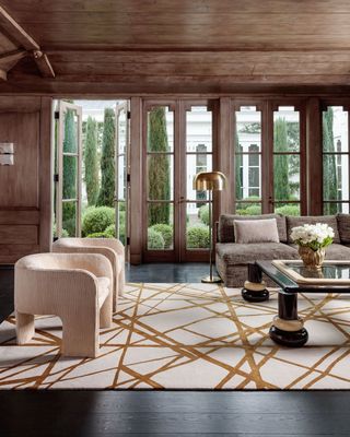 graphic white rug with gold stripes and curved white armchairs in a large living room
