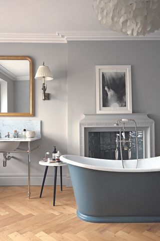 A green rolltop bath in a bathroom with herringbone flooring and a traditional fireplace