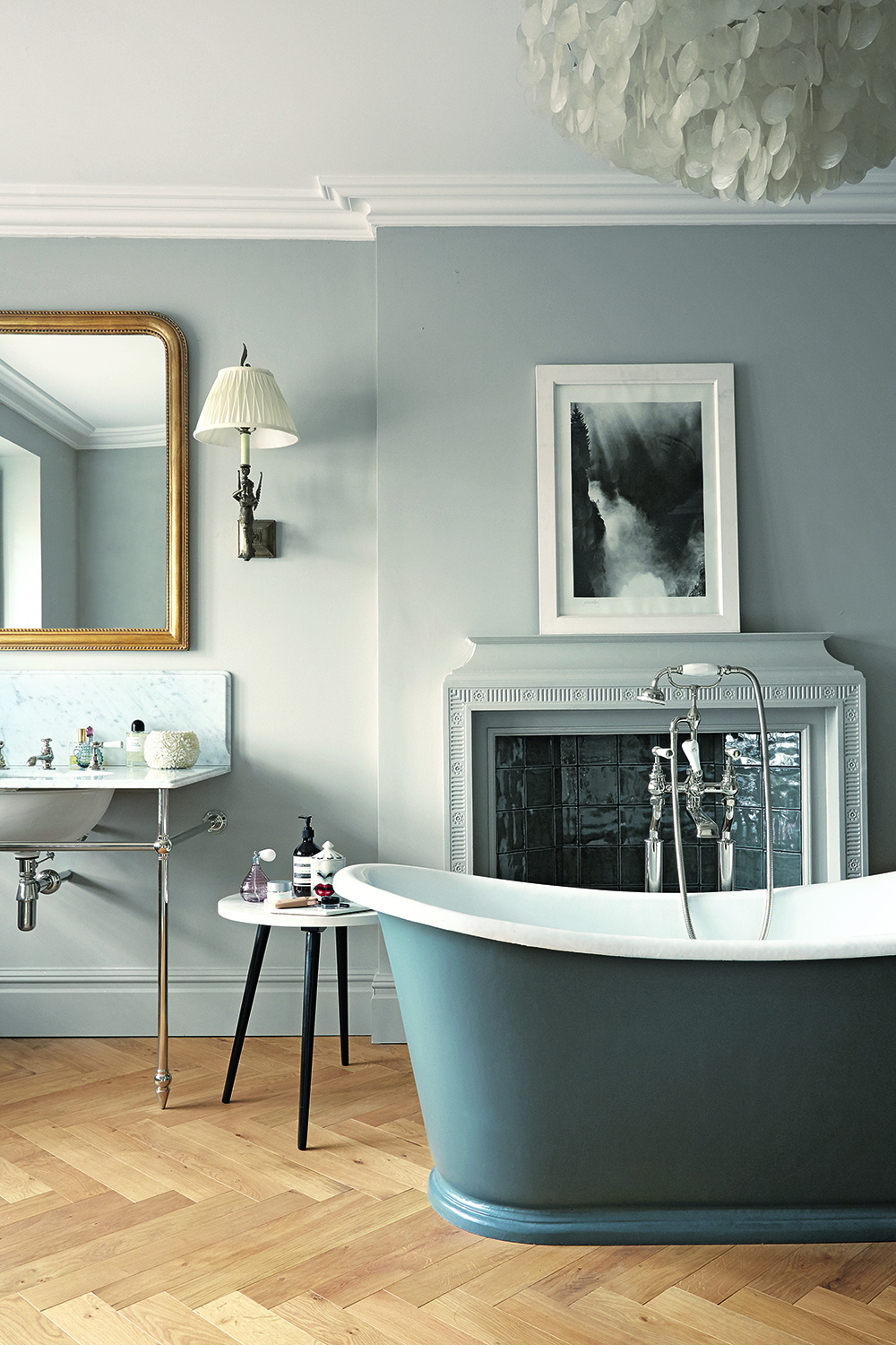 A green rolltop bath in a bathroom with herringbone flooring and a traditional fireplace