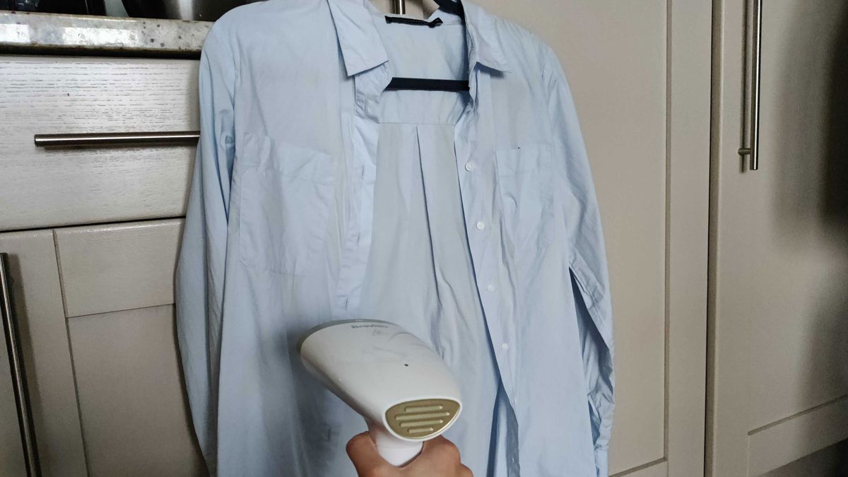 Image shows a light blue Oxford shirt being steamed with a garment steamer.