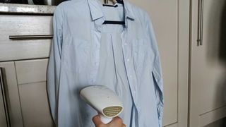 Image shows a light blue Oxford shirt being steamed with a garment steamer.