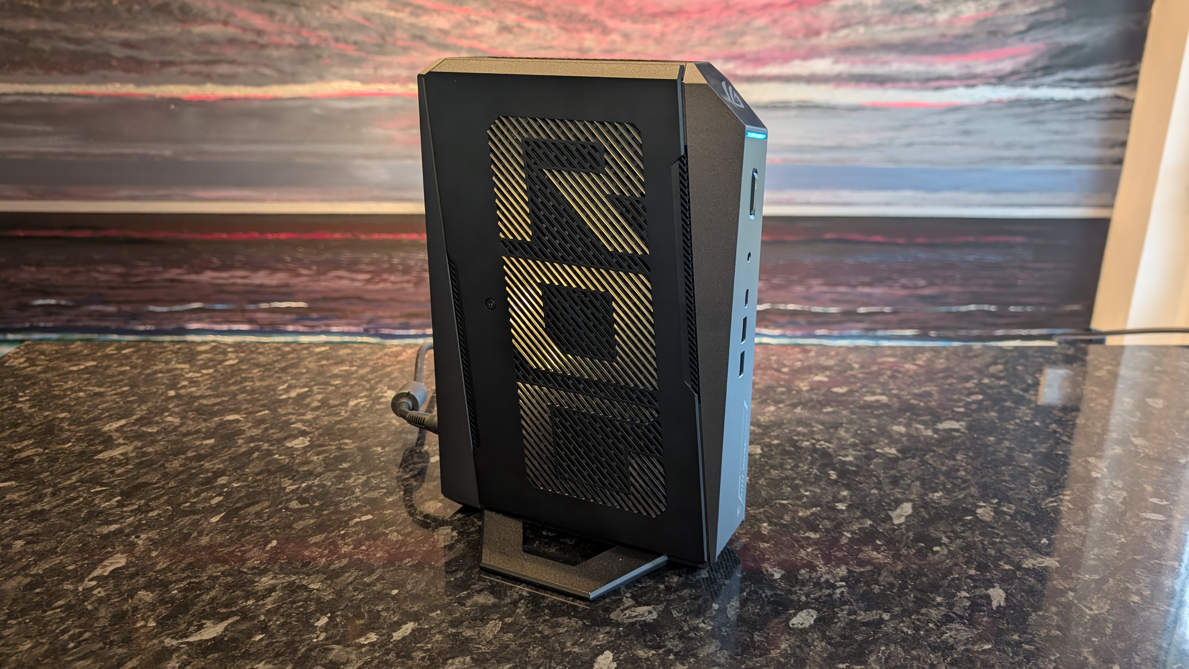The Asus ROG NUC photographed on a dark marbled worksurface with a painted sunset in the background.