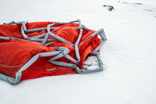 View of a dismantled orange and white tent by 66°North and Heimplanet pictured outside on snow covered ground