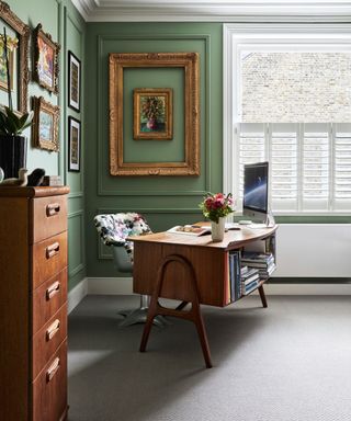 Home office with antique desk, green walls, neutral flooring and shutters on window