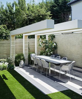 How to lay a patio in a modern scheme with long white table and chairs and architectural pergola-style features.