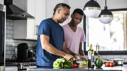 A father and son are in the kitchen cooking with healthy ingredients.