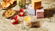 A marble countertop with a lit glass candle beside glasses of red drinks and bowls of appetizers