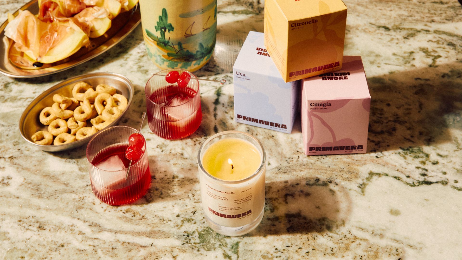 A marble countertop with a lit glass candle beside glasses of red drinks and bowls of appetizers
