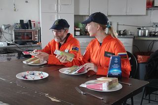 Mars 160 crewmembers Jon Clarke and Anastasiya Stepanova get ready to dig into some Russian space food for dinner.