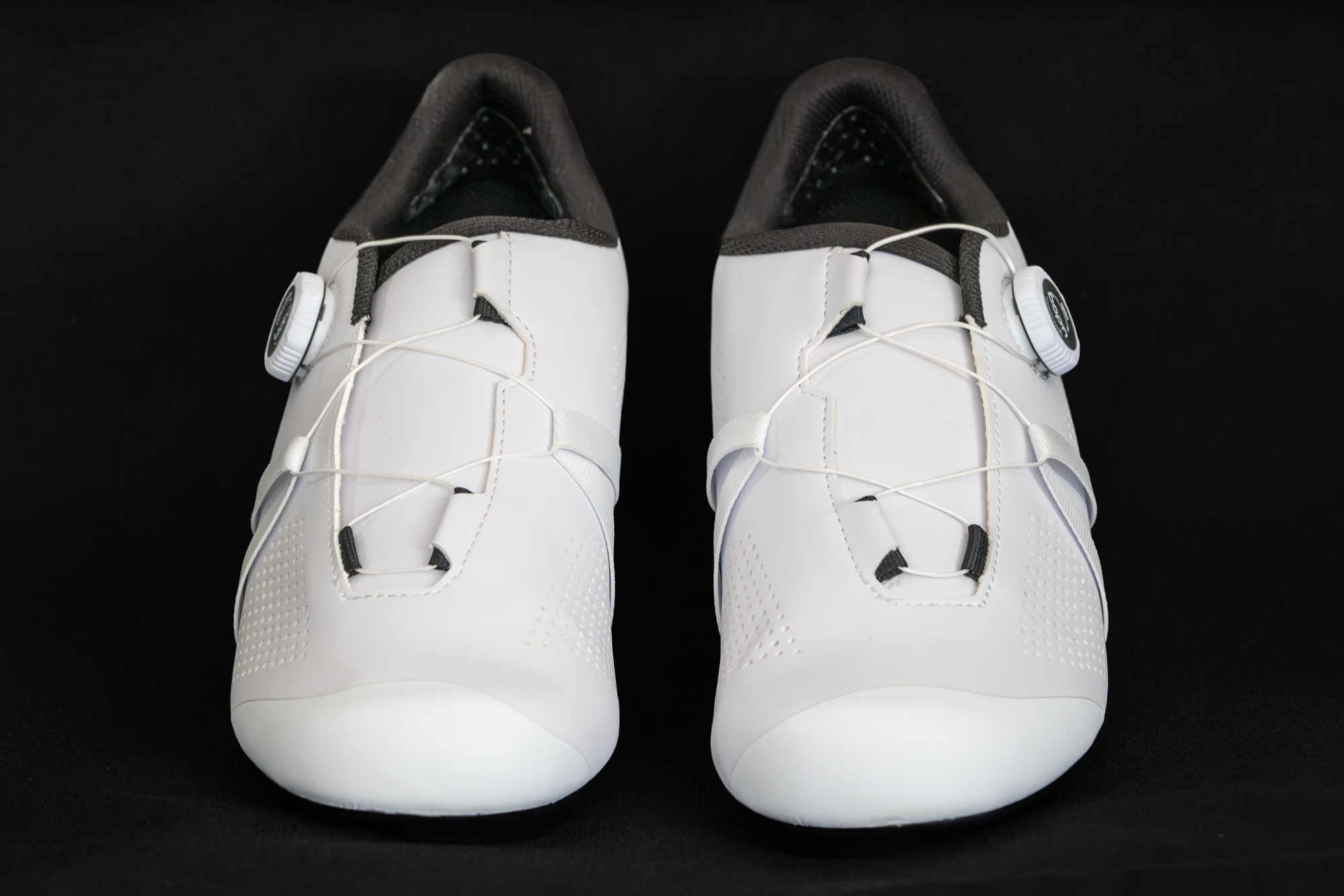front view of a pair of white cycling shoes against a black background