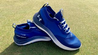 Under Armour Charged Phantom SL Golf Shoe and its blue mesh upper resting on the golf course