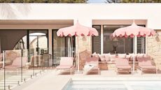 a pool outside a modern house with striped sun loungers and pink parasols