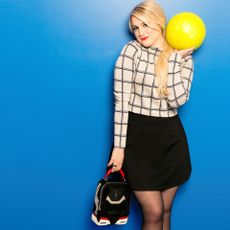 Meghan Trainor simles as she holds up a bright yellow bowling ball.