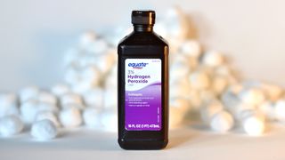 A bottle of hydrogen peroxide with cotton balls in the background