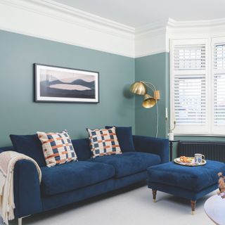 living room with green walls and white ceiling and shutters with blue velvet sofa and footstool