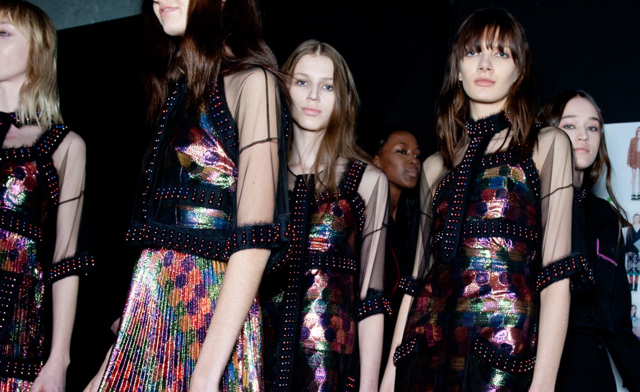 six female models facing in different directions wearing black dresses with bright multicolored details