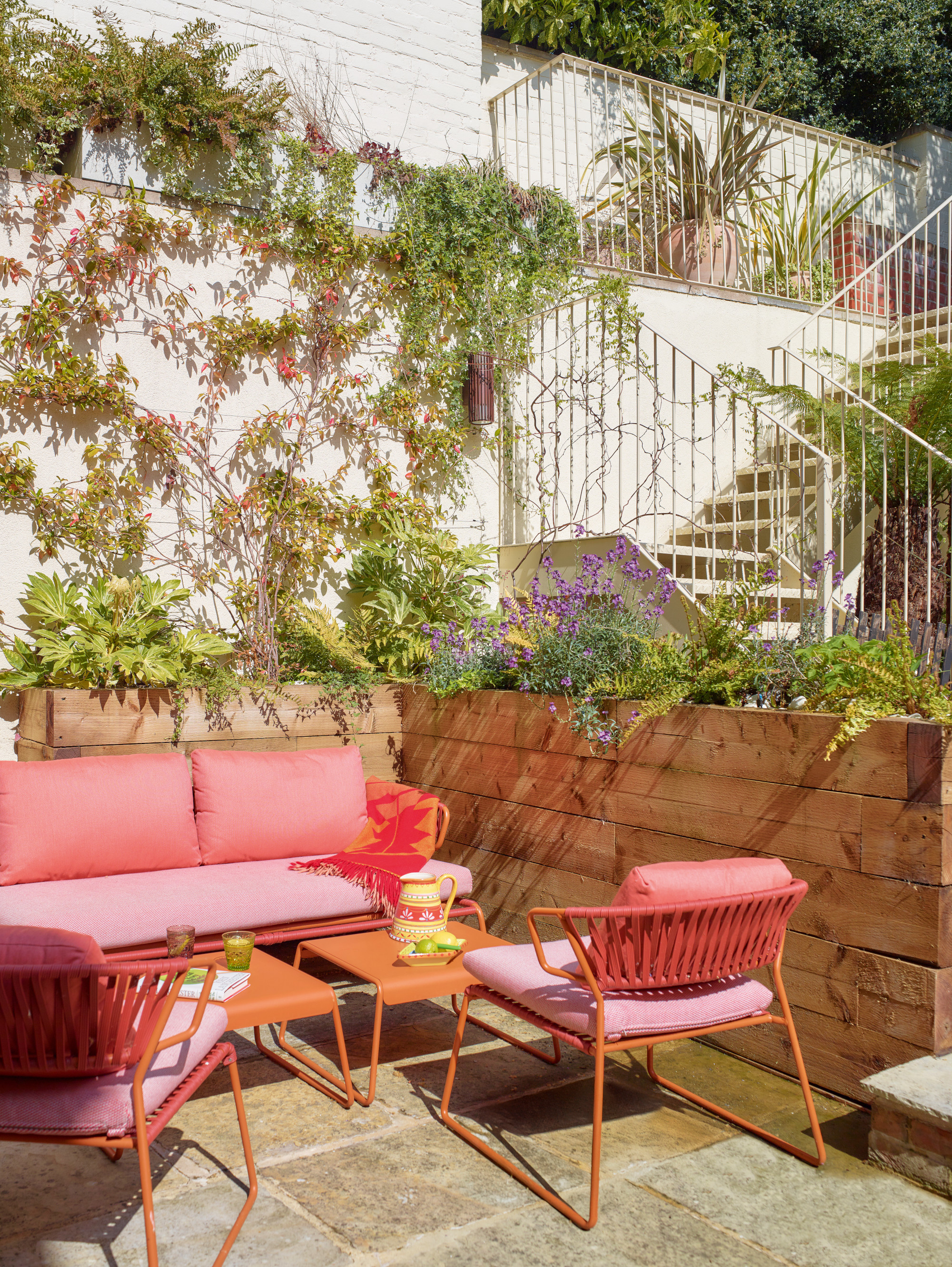 Garden with raised beds, pink and orange garden furniture and white stairs leading up to a second level