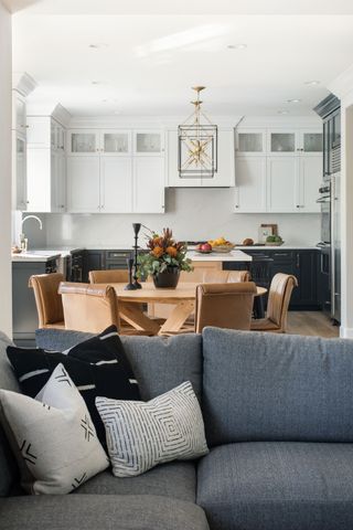 living kitchen diner with gray sofa and wood round table with white and dark cabinets behind and lantern pendant lights