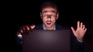 Businessman staring at laptop with frightened face in the dark