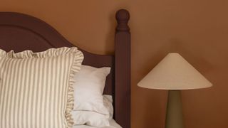 A bedroom with a brown wall, a dark wood bed with stripe duvet and a green and cream lamp