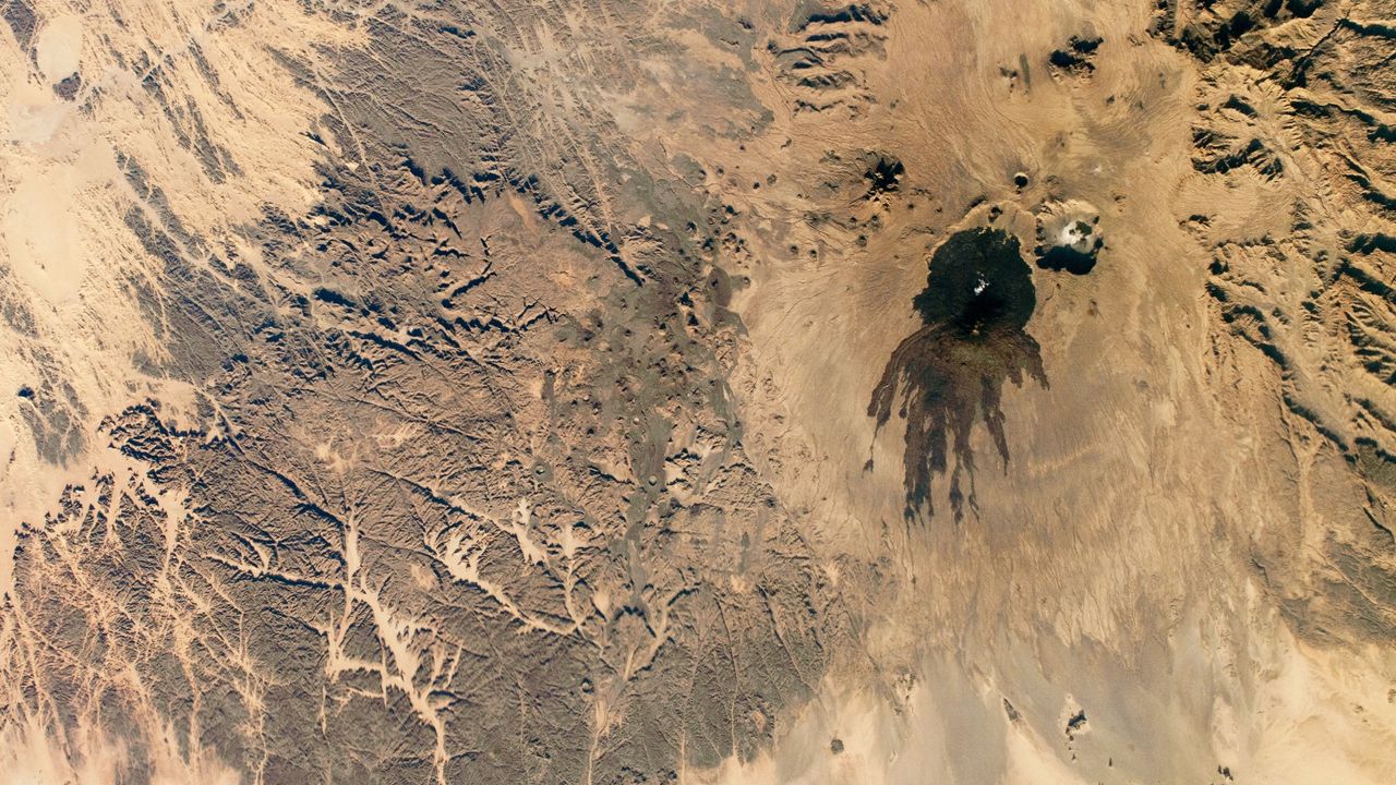 Shadowy tendrils of ancient lava have scarred a dark volcano next to a 'skull' in the Sahara — Earth from space