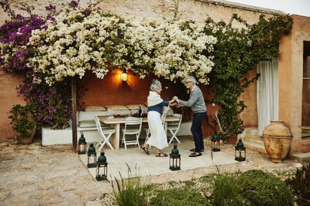 Wide shot of senior couple dancing in garden of tropical villa at sunset while on vacation in Morocco