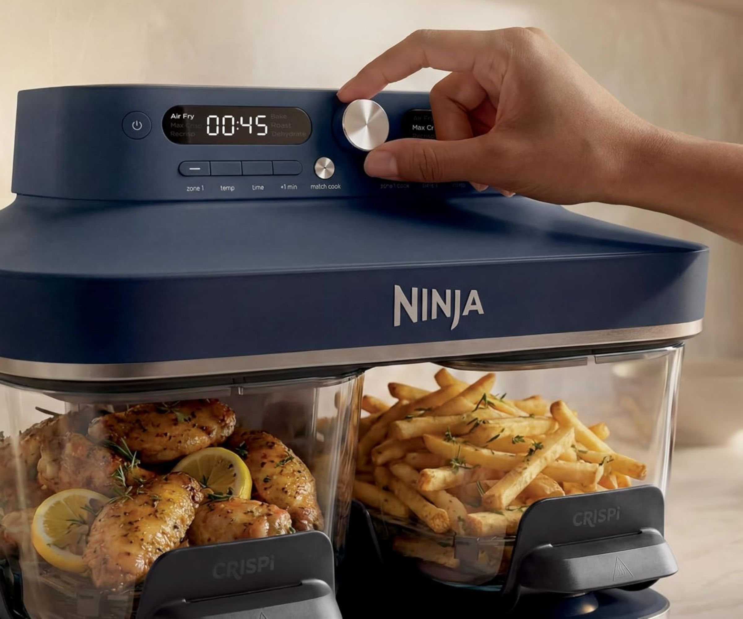 A dark blue Ninja Crispi DualZone Air Fryer with someone adjusting the timer dial