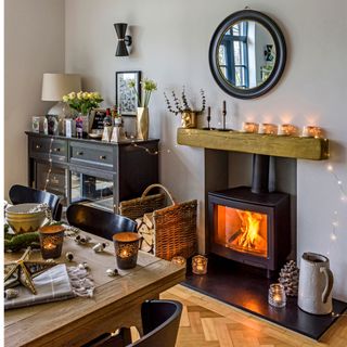 A dining room with table and chairs, a lit fire in a woodburning stove and Christmas candles and decorations