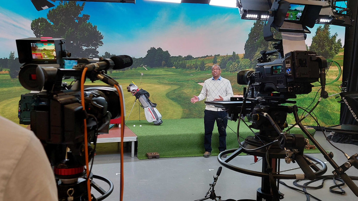 A man stands in front of a green wall in a virtual production studio.